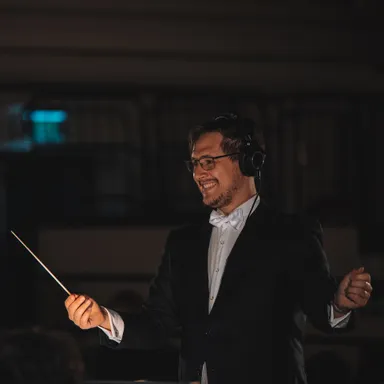 Nathan conducting the Woodville Concert Band, smiling while standing in front of the ensemble with his arm outstretched.